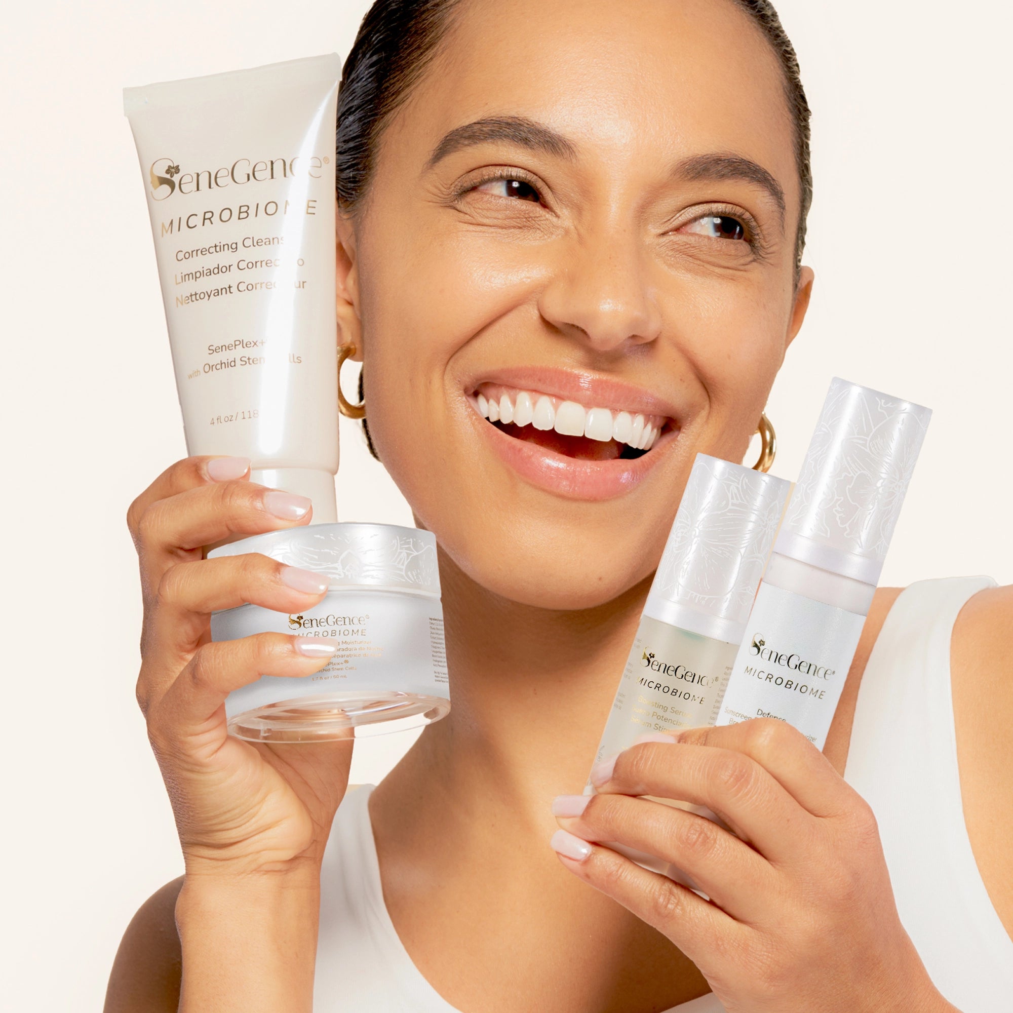 A smiling woman holds the four Microbiome Collection formulas: Correcting Cleanser, Boosting Serum, Defense Daytime Moisturizer SPF 15 and Restorative Evening Moisturizer.